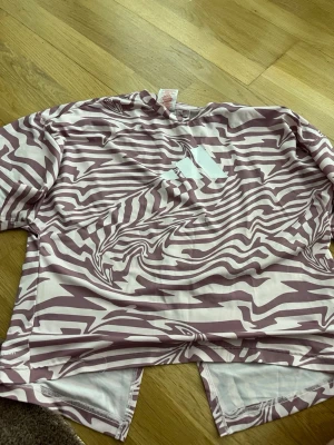 Adidas träningströja zebramönster - Säljer en Adidas träningströja i storlek 164 med ett unikt zebramönster i lila och vitt. Tillverkad i ett lätt och snabbtorkande material, perfekt för träning eller sportaktiviteter. Tröjan har korta ärmar och rund hals.