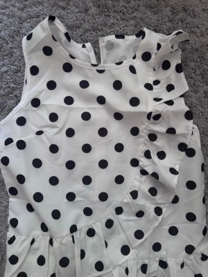 Vit prickig blus med volangdetalj - Snygg ärmlös blus i vit med svarta prickar.