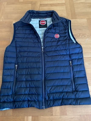 Mörkblå dunväst från Colmar - Snygg mörkblå dunväst från Colmar med quiltad design och två dragkedjeförsedda fickor framtill. Västen har hög krage och Colmar-logga på bröstet samt en mindre logga bak. Perfekt för lager-på-lager och riktigt stilren look.