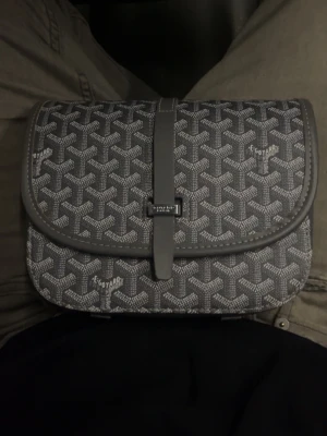 Grå mönstrad handväska med lock - Snygg grå handväska med klassiskt grafiskt mönster och lockstängning. Väskan har en justerbar rem och detaljer i grått konstläder. Perfekt storlek för det viktigaste och ger en trendig touch till din outfit.