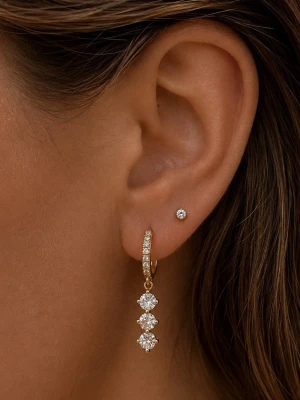 Guldörhänge med tre gnistrande stenar - Säljer ett elegant örhänge i guld med tre stora, gnistrande stenar i rad som hänger från en tunn creol dekorerad med små stenar. Örhänget har en lyxig och modern look som verkligen drar blickarna till sig.