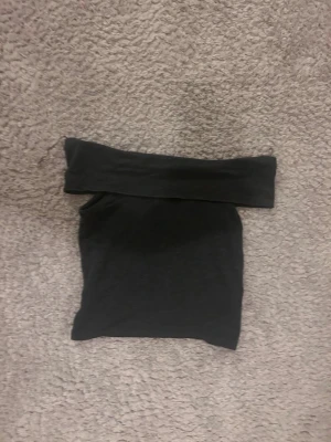 Gråsvart offshoulder topp - Snygg gråsvart offshoulder topp med tight passform. Perfekt att styla med jeans eller kjol för en trendig look. Toppens material känns mjukt och stretchigt, vilket gör den bekväm att bära hela dagen.