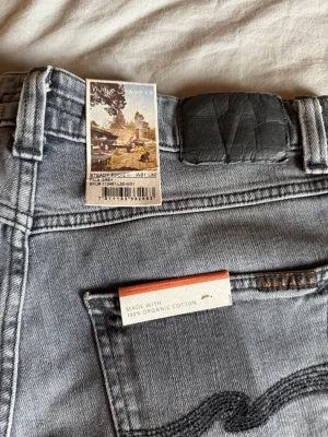 Nudie Jeans Steady Eddie II (Pale Grey) – W31 L32 – Helt nya med lappar! - Säljer ett par grå jeans från Nudie Jeans Co i modellen Steady Eddie II. Jeansen är tillverkade av 100% ekologisk bomull och har klassisk femficksdesign, svarta detaljer och en snygg tvättad look. Perfekta för en avslappnad och trendig stil.