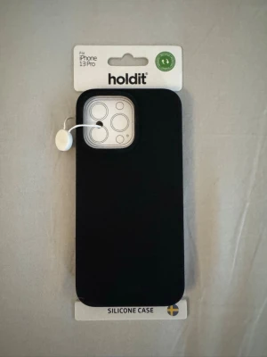 Holdit iPhone 13 Pro skal - Jag köpte fel skal till min nya mobil. Snyggt svart mobilskal från Holdit, gjort i mjukt silikon som ger ett bra grepp och skyddar din iPhone 13 Pro. Skalet har en stilren design med öppning för kamera och knappar. Perfekt för dig som vill ha ett enkelt och stilrent skydd till mobilen.