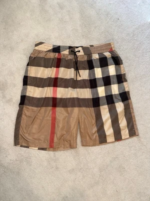 Burberry shorts - Snygga Burberry shorts i storlek XL. Helt oanvända och i nyskick. Eftersom det är badshorts sitter de mer som en L, så kolla gärna måtten innan köp. Stilren Burberry-design och perfekta för sommaren, stranden eller semestern. Aldrig använda och helt rena.  Storlek: XL (passar mer som L)   Skick: Helt ny / oanvänd 