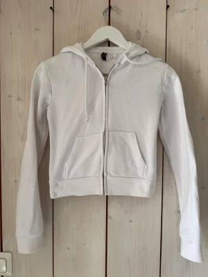 Vit zip hoodie med huva - Säljer en stilren vit hoodie med dragkedja framtill och två fickor. Hoodien har långa ärmar, ribbade muddar och en klassisk huva med dragsko. Perfekt för en avslappnad och enkel look. Materialet känns mjukt och bekvämt. Diffus fläck på ärmen enl. Bild. 