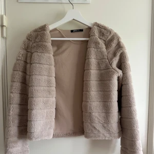 Beige pälsjacka från Gina Tricot XS - Säljer en fluffig och snygg beige pälsjacka från Gina Tricot i storlek XS. Jackan har horisontella sömmar som ger en cool struktur och är helfodrad på insidan. Perfekt för dig som vill ha en mysig och trendig look.