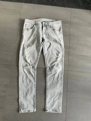 Dondup jeans - Jeansen passar även w32 fast storleken är w35. Säljer ett par ljusgrå jeans i slim fit med slitna detaljer på framsidan. Jeansen har klassisk femficksdesign och är tillverkade i bomull. Perfekta för en avslappnad och trendig look.