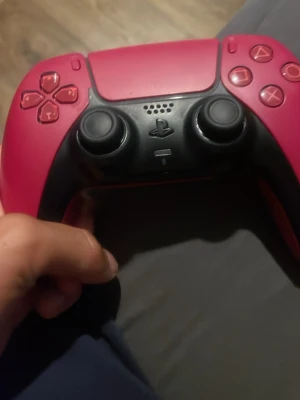 Röd PlayStation 5 DualSense handkontroll - Säljer en snygg röd PlayStation 5 DualSense handkontroll från Sony. Handkontrollen har svart mittparti, två analoga spakar, touchpad och klassiska PlayStation-knappar. Ergonomisk design i plast som passar perfekt för gaming.