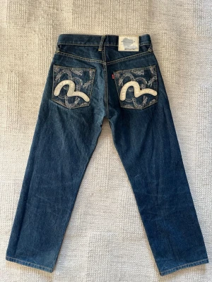 Evisu mörkblå jeans storlek 30 vintage - Sjukt snygga Evisu jeans i en ovanlig vintage modell med drakmönster på fickorna. storlek 30/28 lite osäker på längden men ni kan se längden på bild