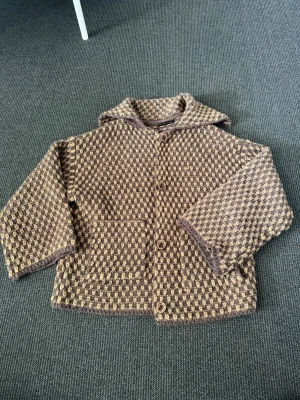 Zara Jacka - Säljer en brun och beige rutig jacka i ull med stora knappar framtill och två fickor. Jackan har en boxig, loose passform och lång ärm. Perfekt för höst och vinter när du vill ha något både snyggt och varmt. 