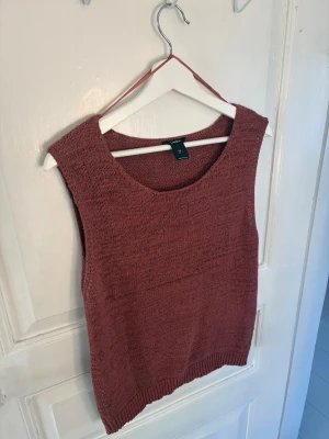 Rostbrun stickad väst från Lindex - Säljer en snygg rostbrun stickad väst från Lindex. Västen har rund halsringning, ärmlös design och ribbstickad nederkant. Perfekt att styla över en skjorta eller t-shirt för en trendig lager-på-lager-look.