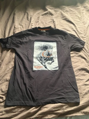 Svart t-shirt med hästmotiv  - Svart t-shirt med tryck av en springande häst i gråskala och orange detaljer.' i orange. Klassisk passform och rund halsringning. Perfekt för dig som gillar unika prints och exklusiva märken.