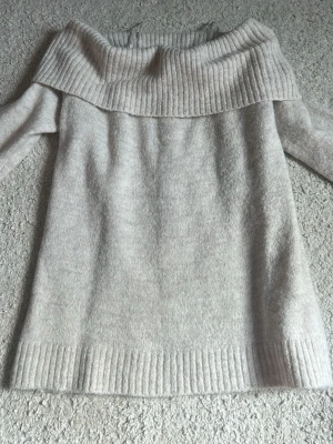 Ljusgrå off shoulder stickad tröja - Mysig ljusgrå stickad tröja med bred ribbad off shoulder-krage och långa ärmar. Tröjan har även ribbade muddar vid ärmslut och nederkant. Perfekt för lager-på-lager och en chill look.