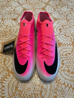 Nike fotbollsskor - Snygga fotbollsskor från Nike i en stark rosa färg med svart swoosh på ovansidan. Skorna har snörning, låg profil och ovandel i syntetmaterial för bra bollkontroll. Perfekta för dig som vill sticka ut på planen och ha grym känsla i spelet.