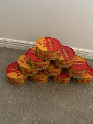 1st, Surströmming Röda Ulven burkar - Flera burkar surströmming från Röda Ulven. Burkarna är runda och har en röd och gul design med text och en röd varg på locket. Perfekt för dig som vill testa klassisk svensk surströmming eller bjuda på en unik matupplevelse.