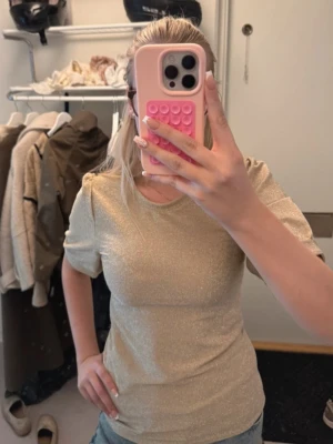Glittrig guld topp med puffärm - Snygg glittrig topp i guld med puffiga korta ärmar och rund halsringning. Jag har sytt in midjan / passformen själv så trots att det står storlek L så anser jag att den numera är liten M/S. 