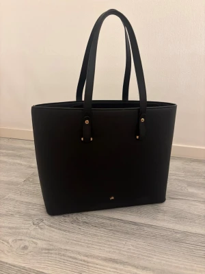 Svart toteväska från Anna Field - Säljer denna stilrena svarta toteväska från Anna Field, köpt på Zalando. Säljes då den tyvärr inte kommer till användning.  Väskan är i fint skick, men har en liten defekt vid öppningen på ena sidan, vilket syns på den tredje bilden. I övrigt är väskan hel och fin.  Mått: • Höjd: ca 30 cm • Bredd: ca 42 cm • Vidd: ca 12 cm