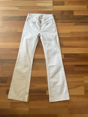 Vita bootcut jeans från Nelly - Snygga vita bootcut jeans från Nelly med hög midja och dubbla knappar framtill. Jeansen har klassiska fickor fram och bak samt kontrastsömmar. Perfekta för dig som vill ha en clean och trendig look.            OBS! Upplagda för kroppar som är 160/162 cm!