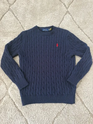 Mörkblå kabelstickad tröja Polo Ralph Lauren - Säljer en superfin och klassisk kabelstickad tröja från Polo Ralph Lauren i mörkblått med röd broderad logga på bröstet. En tidlös stilren modell som passar till allt!  Märke: Polo Ralph Lauren  Färg: Mörkblå (Navy) med röd logga  Modell: Kabelstickad (Cable-knit crewneck)  Storlek: S (syns på lapp i nacken)  Skick: Mycket gott skick / sparsamt använd (justera om det finns något slitage) skriv om ni ska ha mått! 