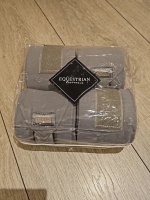 Gråa fleecelindor Equestrian Stockholm - Säljer ett set med fyra gråa fleecelindor från Equestrian Stockholm. Bandagen har snygga detaljer i silver och kommer i en genomskinlig förpackning. Perfekta till hästträning eller tävling. Aldrig andvända, inte ens öppnade. Storlek 4M