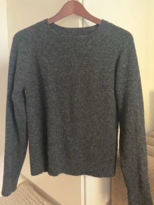 Mörkgrå stickad tröja Vero Moda - Mysig mörkgrå stickad tröja från Vero Moda i storlek XS. Tröjan har rund halsringning, långa ärmar och ribbade muddar vid ärmslut och nederkant. Perfekt för kyliga dagar och enkel att matcha med olika outfits. Typ aldrig använd