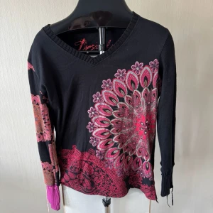 Svart stickad tröja med mönster Desigual - Unik svart stickad tröja från Desigual med färgstarka mandala-inspirerade mönster i rosa, rött och orange. 0419