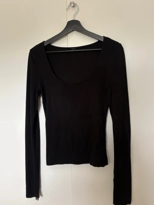 Svart långärmad topp från Gina tricot - Populär topp från Gina. En enkel och stilren svart långärmad topp med djup rundad halsringning. Toppen har en tight passform och är tillverkad i ett mjukt, stretchigt material som sitter snyggt på kroppen. Passar xs-m 