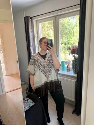Beige poncho med brunt mönster och fransar - Säljer en beige poncho med brunt geometriskt mönster och långa bruna fransar längs nederkanten. Ponchon har v-ringning och vida ärmar, perfekt för lager på lager och en chill look. Materialet känns mjukt och bekvämt. Från märket Odd Molly i storlek 1/2 som enligt deras storlekguide motsvarar en storlek M. Jag har vanligtvis en 4/XL. Passar mig som är en XL. Mycket fint skick, jag hittar inga synliga anmärkningar eller defekter.  