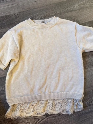 Beige stickad tröja med spetskant - Söt beige stickad tröja med korta ärmar och rund halsringning. Tröjan har en unik detalj med vit spetskant längst ner. Nypris är 500kr