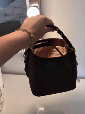 Handväska - 🤎 Helt ny brun handväska 🤎  Säljer denna fina och trendiga väska i mörkbrun mockaliknande finish. Väskan är helt oanvänd och i nyskick då jag fick den i present, men den kom tyvärr aldrig till användning.  ✨ Elegant design med dekorativt handtag ✨ Avtagbart och justerbart axelband medföljer ✨ Rymlig nog för dina vardagsmåsten ✨ Perfekt till både vardag och fest  Inga skador eller anmärkningar – helt ny.  💌 Svarar snabbt på meddelanden och skickar snabbt efter köp. Hör gärna av dig vid frågor. 