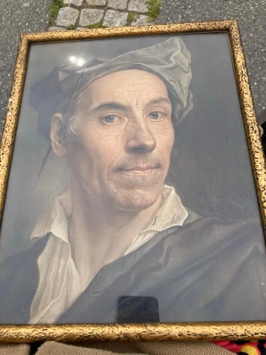 Porträttmålning i guldram - Säljer en klassisk porträttmålning av en man med hatt, inramad i en dekorerad guldfärgad ram. Tavlan har realistiska detaljer och motivet bär en vit skjorta och mörk kappa. Perfekt som unik väggdekoration för dig som gillar konst och historia.