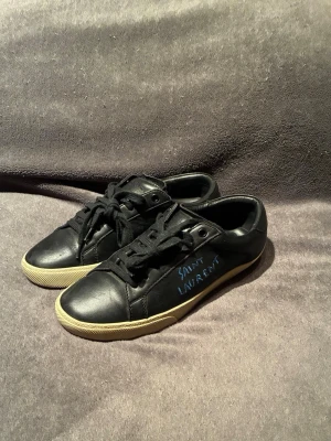 Saint Laurent SL/06 Sneakers - Skor från Saint Laurent | Storlek: 39 kan passa 40 | Färg: Svart med mörkblå text | I fint skick | Skriv vid frågor |