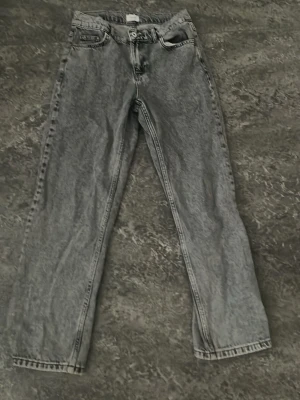 Grå  jeans - Säljer ett par grå tvättade jeans med rak passform och klassisk femficksdesign. Jeansen har hög midja och raka ben, samt detaljerade sömmar och bälteshällor. Perfekta för en avslappnad och trendig look.