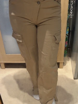 Beiga cargobyxor med fickor - Beige cargobyxor med fickor där bak som är fejka. Alla andra fickor är äkta. med slits 36/38