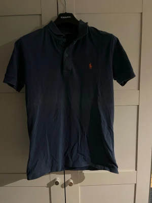 Blå pikétröja med broderad logga - Snygg blå pikétröja från Ralph lauren med korta ärmar och klassisk krage. Tröjan har knappar framtill och en liten broderad logga på bröstet. storlek L i barnstrorlek men sitter som vanlig S/M. Bra skick men behövs strykas. Pris är inte hugget i sten. Hör av er vid frågor!