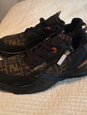 Fendi Flow  - Fendi Flow sneakers. Storlek 44 passar oxå 43. Helt nya icke använda. Köpta i Marbella. Nypris: 4 500kr. Finns tecken på användning som gör att skorna säljs billigt. Men dom är helt felfria och fortfarande snygga!