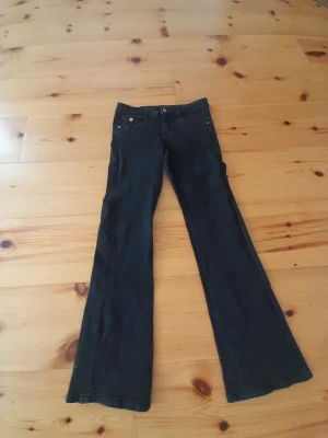 Svarta bootcut jeans - Säljer ett par svarta bootcut jeans med klassisk femficksmodell och utsvängda ben. Jeansen har knapp- och dragkedjestängning samt silverfärgade nitar. Perfekta för dig som gillar en retroinspirerad look.