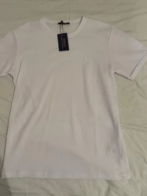 Vit t-shirt från Polo Ralph Lauren - Klassisk vit t-shirt från Polo Ralph Lauren med rund halsringning och diskret broderad logga på bröstet. T-shirten är kortärmad och perfekt för en stilren och enkel look. Storlek är M men passar bäst för S 