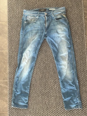 Blå slim fit jeans från Replay - Snygga blå slim fit jeans från Replay med slitna detaljer och klassisk femficksmodell. Jeansen har ljusa tvättade partier och smal passform som ger en modern look. Tillverkade i mjukt denimtyg för skön känsla.