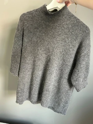 Grå stickad tröja med halvpolo - Mysig grå stickad tröja med halvpolo och halvlånga ärmar. Tröjan har en avslappnad passform och är gjord i ett fluffigt, mjukt material som känns skönt mot huden. Perfekt för lager på lager och enkel att styla till olika outfits. Ord pris 1200kr
