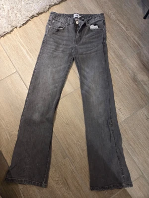 Grå raka jeans med fickdetaljer - Säljer ett par grå jeans med raka ben och klassisk femficksmodell. Jeansen har snygga fickdetaljer bak med knappar och är tillverkade i denim. Perfekta för en avslappnad och trendig look.