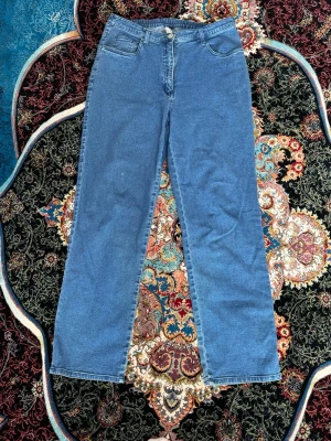 Blå raka jeans med hög midja - Säljer ett par klassiska blå jeans med rak passform och hög midja. Jeansen har fem fickor och stängs med dragkedja och knapp. Materialet är denim i bomull och längden är cirka 102 cm. Perfekta till en avslappnad stil.