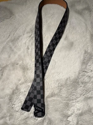 Lv bälte  - Säljer ett stilrent LV-bälte i Damier Graphite med svart LV-spänne. Bältet är i fint använt skick med normalt slitage, se bilder för skick. Passar perfekt till både vardag och fest. 