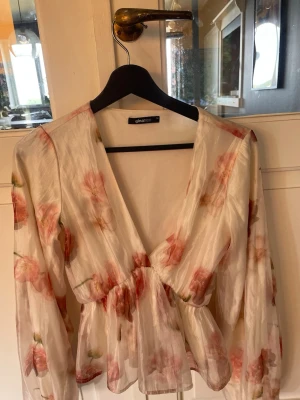 Blommig omlottblus från Gina Tricot - Säljer en superfin omlottblus från Gina Tricot i storlek 34. Blusen är vit med rosa blommönster, har lång ärm och knyts i midjan. Materialet är tunt och lätt, perfekt för en fräsch och romantisk look.