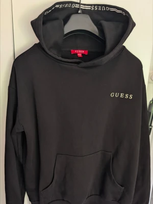 Svart hoodie med huva - En enkel svart hoodie med huva med logo innuti och långa ärmar. Tillverkad i mjukt bomullsliknande material. Insidan av huvan har ett mönstrat tyg som ger en snygg kontrast. Finns katt i hemmet och kan finnas spår. Känns lite blekt under armhålorna men annars inget att anmärka. 