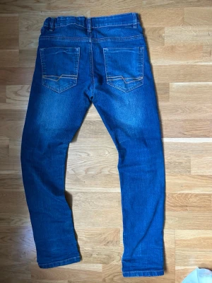 Blå slim fit jeans med slitningar - Snygga blå slim fit jeans med lätt slitna detaljer och klassiska fem fickor. Jeansen har normal midja, raka ben och kontrastsömmar. Perfekta till vardagslooken och passar till det mesta. Tillverkade i mjukt denimtyg för skön känsla.