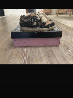 Nike SB dunk (Travis Scott) - Unika sneakers i svart och beige med paisleymönster och tjocka vita snören. Skorna har perforerad tåbox och detaljer i mocka och canvas. Snygg kontrast mellan färgerna och cool design som sticker ut.