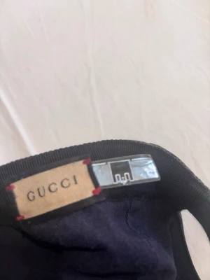Gucci keps med GG-mönster - Säljer en snygg Gucci keps i klassiskt beige och brunt GG-mönster med svart skärm och röd-grön rand på sidan. Kepsen är i tygmaterial och har justerbar rem bak. Perfekt för dig som vill ha en exklusiv och trendig accessoar. En tvätt och knappen där uppe saknas, annars felfri! Självklart äkta pris kan diskuteras😆
