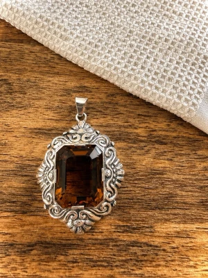 Vintage silver hänge med brun sten - Unikt hänge med en stor, rektangulär brun sten infattad i en detaljerad silver ram med snirkliga mönster. Hänget har en klassisk och elegant look som sticker ut och passar perfekt till dig som gillar statement-smycken. Tillverkare: Per Emilson, Laholm 1948. Vikt :ca 21 g